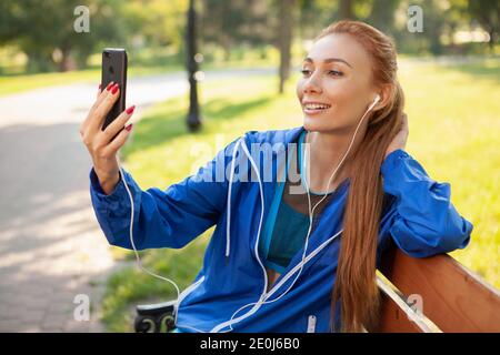 Charmante jeune femme heureuse dans les vêtements de sport en utilisant son smartphone dans le parc après l'exercice, copier l'espace. Des appels vidéo de femme joyeuse avec h Banque D'Images