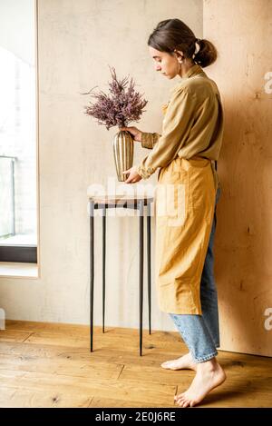 Femme décorant la maison avec une fleur de Calluna séchée dans un vase doré sur fond de mur beige Banque D'Images