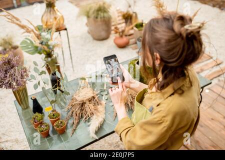 Femme photographiant sur un smartphone des compositions de fleurs et d'herbes lors d'un atelier floral à l'extérieur Banque D'Images