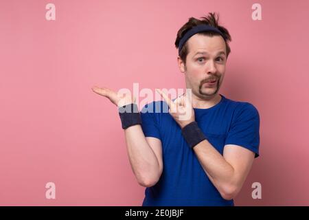 Jeune sportif caucasien drôle d'homme pointant de côté, montrant quelque chose à l'espace vide. Studio tourné sur un mur rose. Banque D'Images