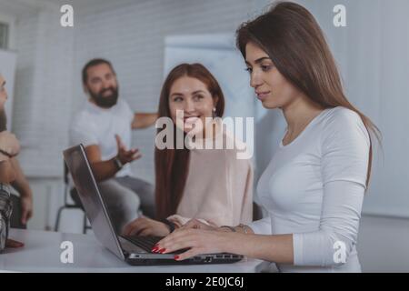 Une femme attirante et sa collègue qui utilisent un ordinateur portable lors d'une réunion d'affaires, un espace de copie. Femmes entrepreneurs travaillant sur ordinateur ensemble à l'o Banque D'Images