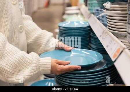 Une cliente choisit et achète des assiettes en argile bleue, un ustensile de dîner pour sa cuisine dans un magasin de produits ménagers ou un supermarché. Concept commercial. Banque D'Images