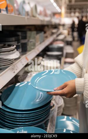 Une cliente choisit et achète des assiettes en argile bleue, un ustensile de dîner pour sa cuisine dans un magasin de produits ménagers ou un supermarché. Concept commercial. Banque D'Images