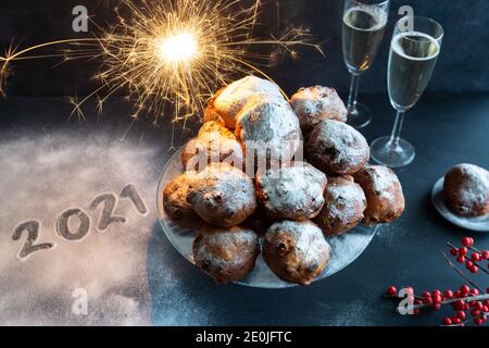 Bonne année avec le sucre glace écrit de l'année 2021 À côté d'un bol d'oliebollen (beignets de pâte hollandais) avec des sparkles et deux verres de champagne Banque D'Images