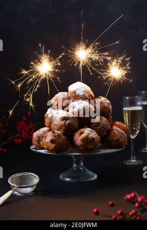 Une pile d'oliebollen hollandaise traditionnelle (traduction : boules de pâte frite) sur un support en verre avec des sparkles et deux verres de champagne Banque D'Images