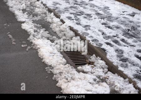 12 - scène urbaine de pas dans un pavé plein de neige. Le drain ressort de l'accumulation de neige sur le côté de la route. Scène environnementale d'hiver Banque D'Images