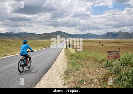 Un cycliste traverse la plaine de Castelluccio tout en observant le paysage environnant. Castelluccio di Norcia, Pérouse, Ombrie, Italie. Banque D'Images