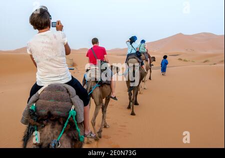 Les touristes étrangers se rendent dans le désert au coucher du soleil à Merzouga, qui se trouve au bord d'Erg Chebbi (la mer de sable) au Maroc. Banque D'Images