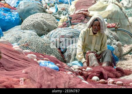 Un vieil homme effectuant des réparations sur un filet de pêche au port d'Essaouira sur la côte océan Atlantique du Maroc. Banque D'Images