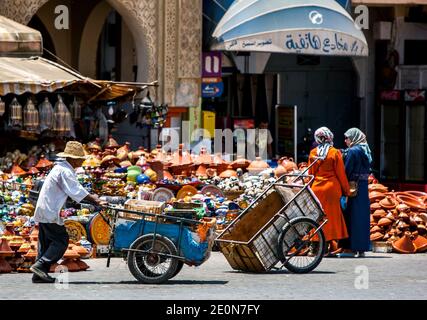 Un homme pousse une voiturette devant une cale sur la place Lahdim, la place principale de la vieille ville de Meknes. Meknes est l'une des quatre villes impériales du Maroc. Banque D'Images