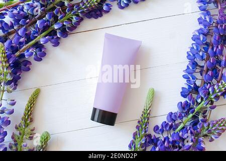 Bouteille de maquette pour marquage et étiquette. Lupin fleurs et maquette / modèle 3d de bouteille souple mauve tube en plastique avec capuchon noir. Vue de dessus. Naturel ou Banque D'Images