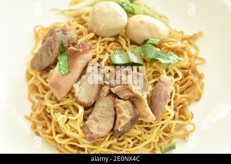 Nouilles aux œufs jaunes chinoises avec garniture de porc braisé et boule assiette avec os dans une tasse à soupe d'herbes brunes Banque D'Images