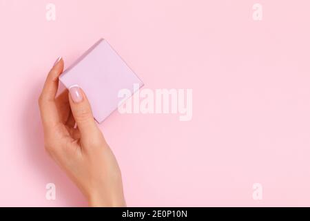 Une main femelle tient une boîte cadeau sur fond rose pastel. Anniversaire Saint-Valentin nouvel an noël. Copier l'espace. Banque D'Images