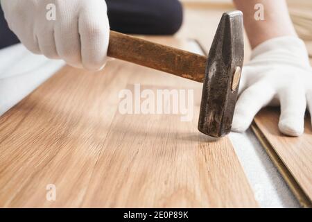 Installation du plancher laminé, détails sur les mains d'homme en gants blancs, en tenant le marteau sur le carrelage en bois, couche de base blanche sous Banque D'Images