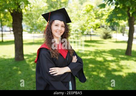 la fille est debout dans le parc vert près de l'université. Elle est diplômée et de bonne humeur Banque D'Images