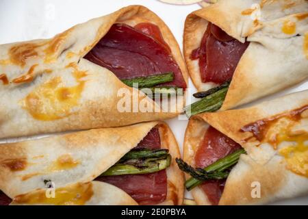 Vue en zénithal macro de certains capots. Canapés au jambon salé avec asperges sauvages enveloppés dans un gâteau au maïs cuit au four. Des aliments frais et sains Banque D'Images