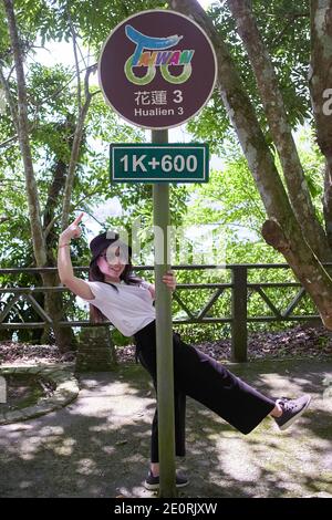 Femme asiatique tenant sur le panneau de la borne de marqueur de distance sur le chemin entourant le lac Carp, Taïwan Banque D'Images