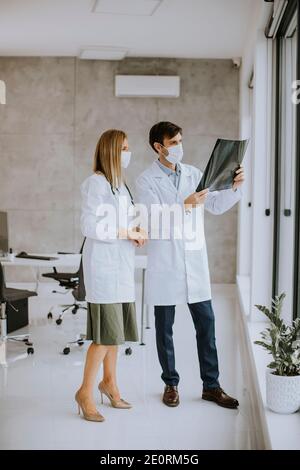 Équipe de médecins avec masques protecteurs pour le visage examinant la radiographie dans le bureau Banque D'Images