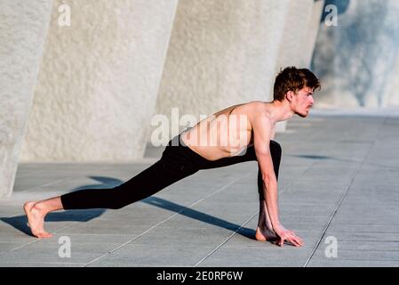 Jeune athlète masculin à poil rouge qui s'étire après l'entraînement pour gagner en flexibilité et détendre ses muscles, à l'extérieur avec un arrière-plan non focalisé. Banque D'Images