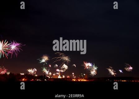 Un énorme feu d'artifice coloré dans la nuit du nouvel an avec maisons et église Banque D'Images