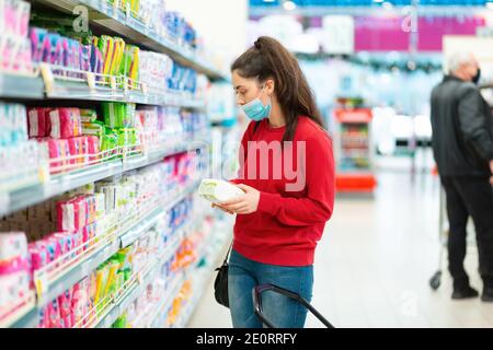 Une jeune femme dans un masque choisit un produit dans un magasin. Le concept de consumérisme et de shopping pendant la pandémie du coronavirus. Banque D'Images