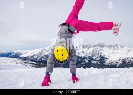 Fille avec des vêtements de ski et un casque sur sa tête, essayez de faire un somersault dans la neige sur le sommet de la montagne, avant de skier sur les pistes. Banque D'Images