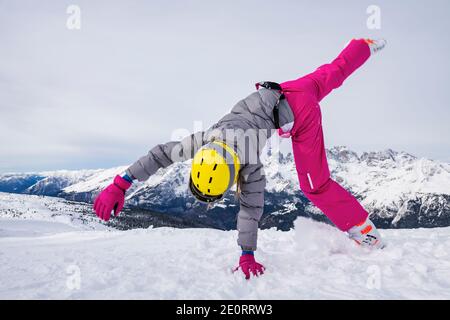 Fille avec des vêtements de ski et un casque sur sa tête, essayez de faire un somersault dans la neige sur le sommet de la montagne, avant de skier sur les pistes. Banque D'Images