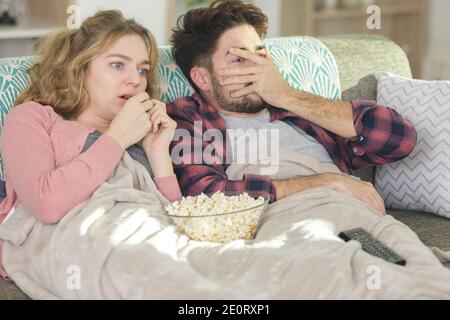 drôle de couple assis sur le canapé regardant le film d'horreur Banque D'Images