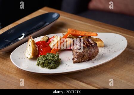 Filet de Mignon sur une assiette noire sur fond de légumes verts, d'épices et de légumes, sur une feuille de cuivre. Gros plan. Banque D'Images