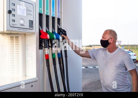 Un homme dans un masque de protection noir prend un pistolet de ravitaillement diesel pour verser le carburant dans le réservoir de la voiture.Traduction- Roubles, litres Banque D'Images