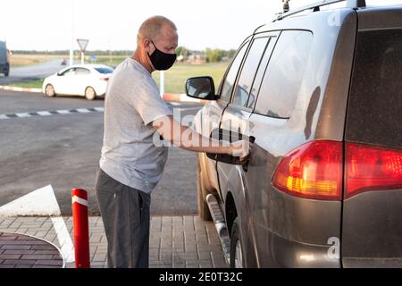 Homme dans un masque de protection noir remplit une voiture de SUV à une station-service, protection contre les virus Banque D'Images