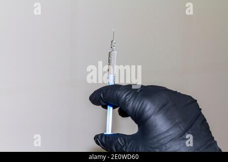 Covid-19: La main de l'infirmière tient une seringue avec le vaccin contre Covid-19 (SRAS-COV-2) dans une main avec un gant noir. Banque D'Images