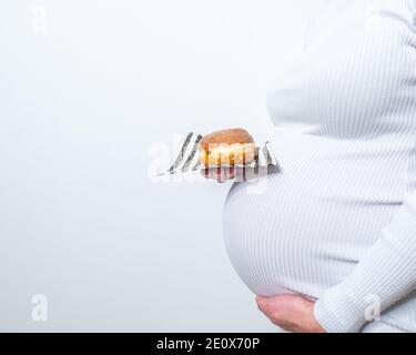 Grossesse et alimentation malsaine concept: La femme enceinte tient une assiette avec des beignets savoureux dans sa main Banque D'Images