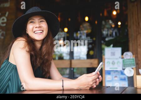 Jeune belle femme asiatique travaillant dans un café loft ou un bureau. Tenir le smartphone pour naviguer sur Internet et effectuer des recherches wi-fi. Femme d'affaires ou pigiste Banque D'Images