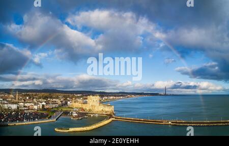 Carrickfergus près de Belfast, Irlande du Nord, Royaume-Uni. Château normand médiéval avec arc-en-ciel, port, brise-lames et ville. Temps orageux dans la lumière du coucher du soleil Banque D'Images