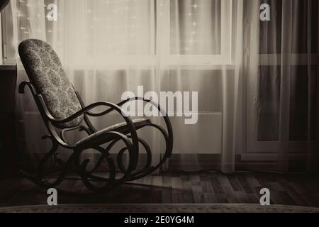 Une chaise à bascule se tient près de la fenêtre dans la lumière du soir. Sépia noir et blanc. Banque D'Images