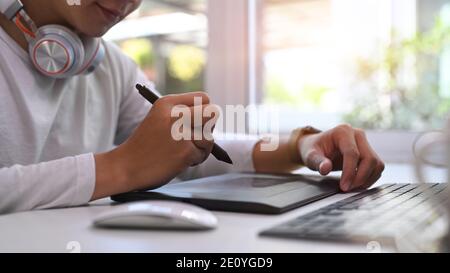 Prise de vue rognée d'un homme de créateur utilisant une tablette sans fil moderne avec clavier et stylet tout en travaillant dans un bureau moderne. Banque D'Images