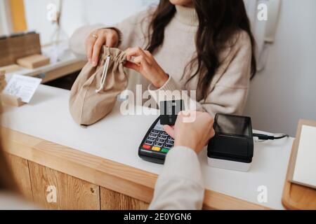 Commerçant mettant des marchandises dans un sac en tissu, femme payant à la main avec une carte Banque D'Images