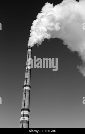 La fumée épaisse s'élève en haut des tuyaux industriels. Pollution de l'environnement par les déchets. Photo en noir et blanc. Banque D'Images