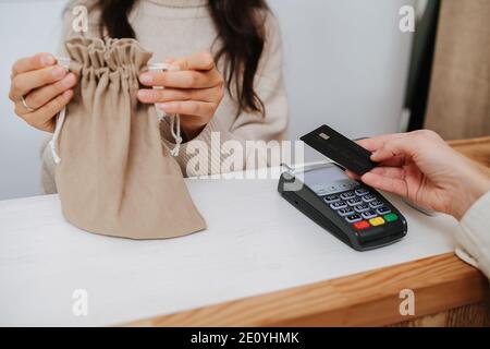 Image rognée d'un commerçant mettant des marchandises dans un sac en tissu pour un client payant Banque D'Images