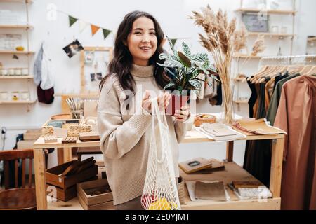 Femme souriante dans un magasin écologique posant pour la photo avec le filet sac et plante en pot Banque D'Images