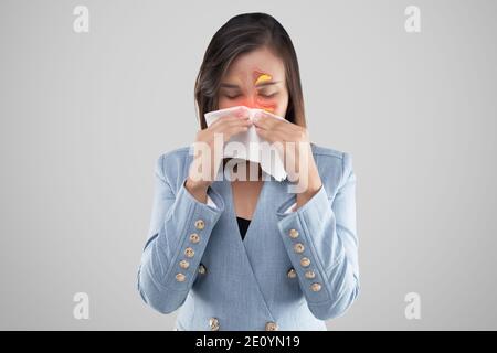 La femme asiatique se sent mal à cause des symptômes des sinus sur fond gris. Femme d'affaires en costume bleu soufflant le nez dans un tissu. Allergie aux acariens. Colonne Banque D'Images