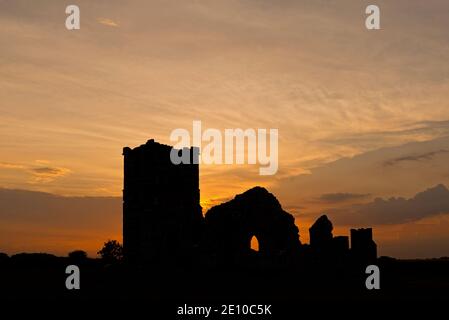 Une photo au coucher du soleil de l'église Knowlton à Dorset, Angleterre, Royaume-Uni, par une journée partiellement nuageux avec la lumière du soleil créant un éclairage intéressant des nuages. Banque D'Images
