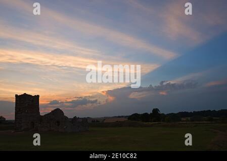 Une photo au coucher du soleil de l'église Knowlton à Dorset, Angleterre, Royaume-Uni, par une journée partiellement nuageux avec la lumière du soleil créant un éclairage intéressant des nuages. Banque D'Images