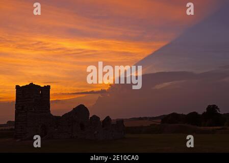 Une photo au coucher du soleil de l'église Knowlton à Dorset, Angleterre, Royaume-Uni, par une journée partiellement nuageux avec la lumière du soleil créant un éclairage intéressant des nuages. Banque D'Images