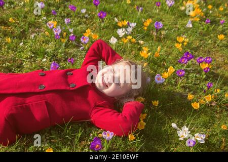 Une petite fille mignonne se trouve dans une forêt florissante, glade avec des fleurs multicolores de printemps crocuses. L'enfant sourit et apprécie le temps du printemps. Banque D'Images