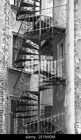 Escalier en acier rotatif ornemental fantaisie (sortie d'urgence) à l'extérieur d'une ancienne maison de résidence à Cracovie, en Pologne. Photo noir et blanc. Banque D'Images