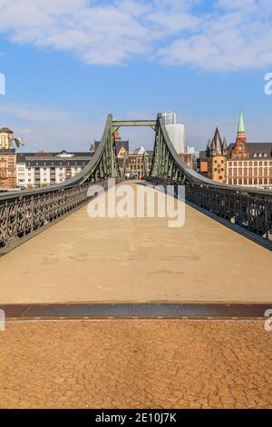 Passerelle historique au-dessus du main à Francfort par jour. Maisons de la vieille ville en arrière-plan avec le soleil et quelques nuages. Pont avec terre en fer Banque D'Images