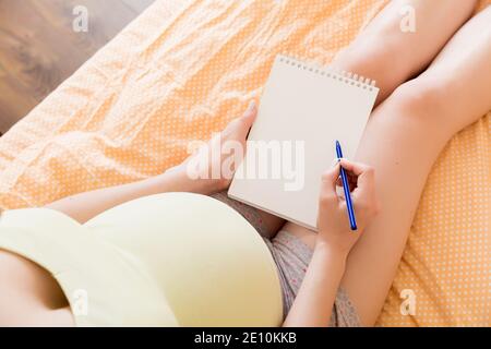 Une femme enceinte prend des notes dans un carnet. Concept de grossesse mère en attente de bébé. Banque D'Images