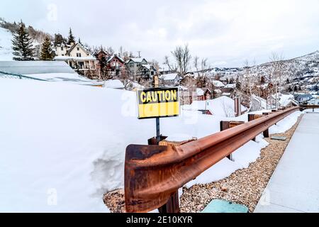 Panneau attention sur la rambarde rouillée d'une route à l'intérieur la montagne enneigée en hiver Banque D'Images